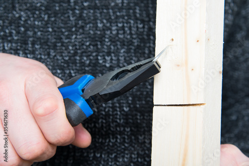 close-up, hand of a worker with pliers, pulling a metal nail from a wooden bar photo