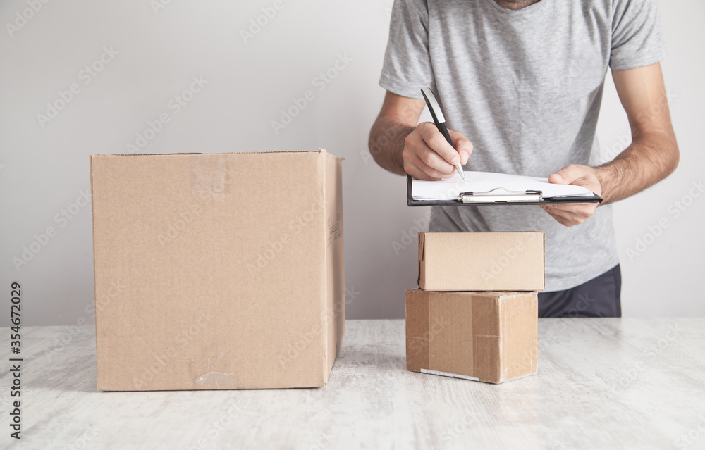 Man writing in clipboard. Cardboard boxes on the desk. Products, Commerce, Retail, Delivery Man writing in clipboard. Cardboard boxes on the desk. Products, Commerce, Retail, Delivery