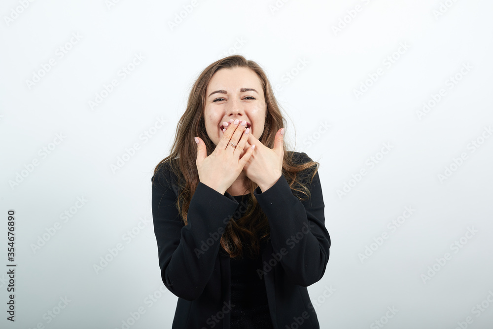 Covering her mouth with hand and gazing while giggling expresses sincere emotions of joy cheerful mood, portrait. Young attractive woman brunette in a black t-shirt, sweater on white background Covering her mouth with hand and gazing while giggling expresses sincere emotions of joy cheerful mood, portrait. Young attractive woman brunette in a black t-shirt, sweater on white background