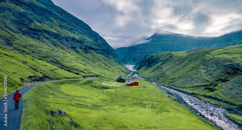 Tourist walking on the trek to Pollurin canyon. Gloomy evening view of Saksun village, Faroe Islands, Denmark, Europe. Harsh beauty of the northern countries. Traveling concept background. photo