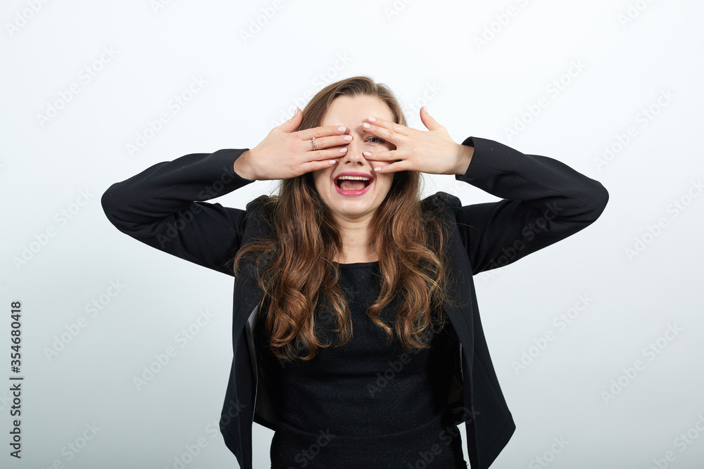 Closing face palms covers her eyes visible through with hands. Young attractive woman brunette in a black t-shirt and sweater on white background Closing face palms covers her eyes visible through with hands. Young attractive woman brunette in a black t-shirt and sweater on white background