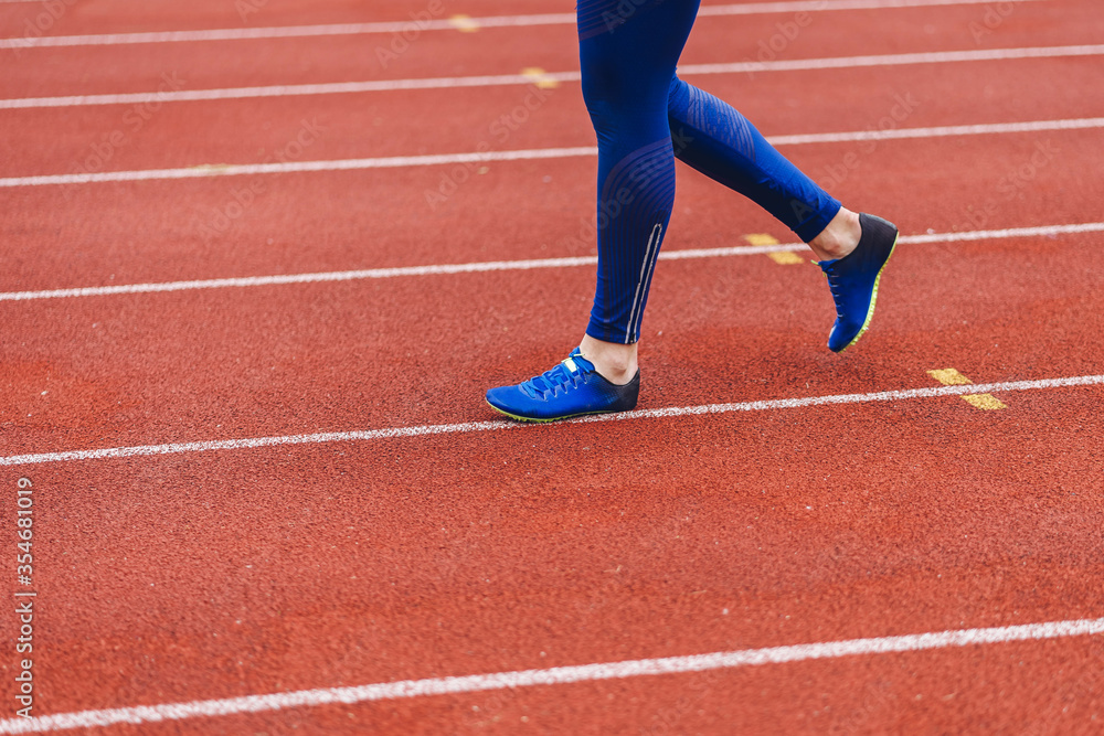 Young fitness woman in blue shoes and blue leggings walking on running court or treadmill. Girl in blue sport wear close-up to shoes running court background. Health exercise life style Young fitness woman in blue shoes and blue leggings walking on running court or treadmill. Girl in blue sport wear close-up to shoes running court background. Health exercise life style