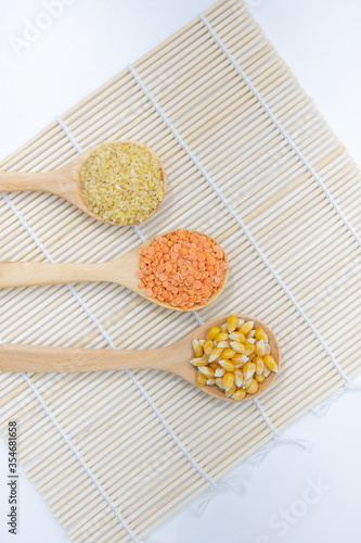 Unprocessed organic Bulgur wheat , Corn , Red split lentils in wooden spoon. Raw Whole grain Dry agriculture ingredients. Healthy super food concept. White background. Selective focus