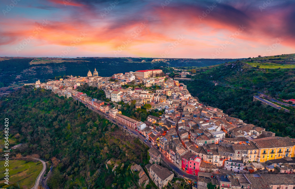 View from flying drone. Dramatic summer sunset in Ragusa town with Duomo San Giorgio - baroque Catholic church on background. Superb evening scene of Sicily, Italy, Europe.