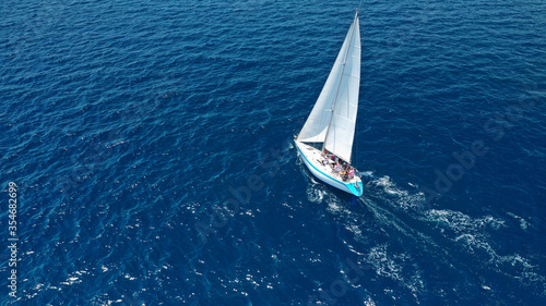 Aerial drone top down photo of beautiful sail boat cruising deep blue Aegean sea