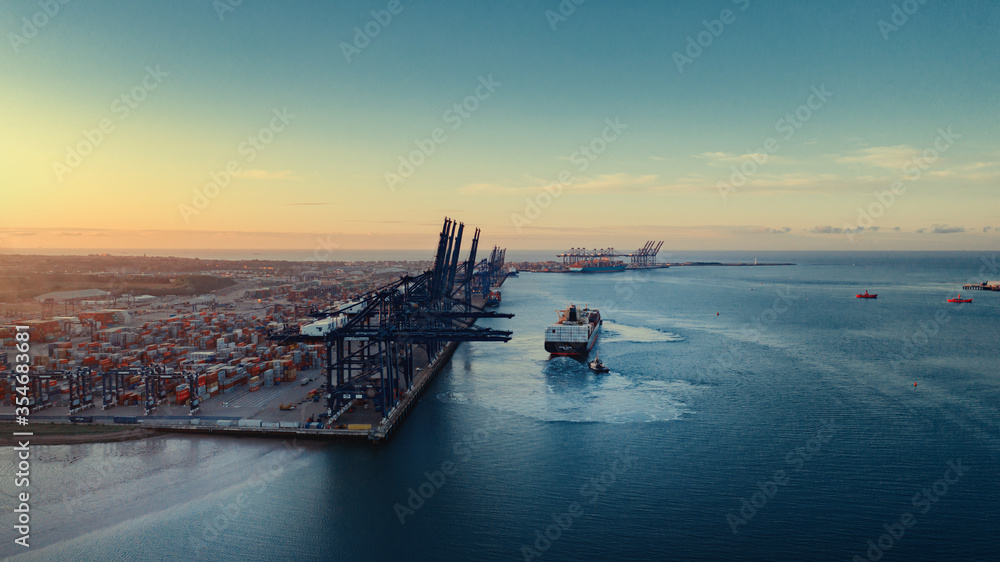 Sunrise over Felixstowe Container Port as two tugs help a container ship to cast off from the harbour wall and make it's way out to sea. - obrazy, fototapety, plakaty 