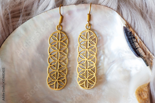 Beautiful sacred geometry brass earrings on shell background photo