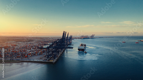 Sunrise over Felixstowe Container Port as two tugs help a container ship to cast off from the harbour wall and make it's way out to sea.