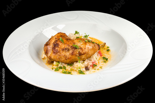 Delicious roasted chicken leg with vegetable risotto on a white plate, isolated on black background