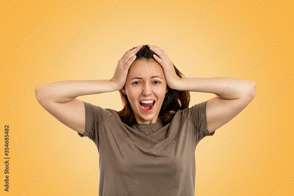 Portrait of an afraided young Caucasian woman holding her hands up on head and shouting. Yellow background. Human emotions, the concept of facial expression Portrait of an afraided young Caucasian woman holding her hands up on head and shouting. Yellow background. Human emotions, the concept of facial expression
