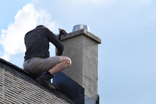 Tela Roofer construction worker repairing chimney on grey slate shingles roof of domestic house, blue sky background with copy space