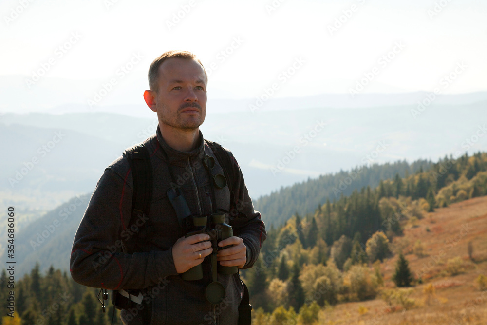 Portrait of a man with a backpack standing on a mountain hill, enjoying natural landscapes Portrait of a man with a backpack standing on a mountain hill, enjoying natural landscapes