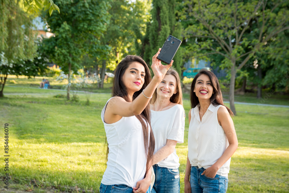 Obraz premium Three multiethnic girls taking a selfie in the park. Young and smiling girls. Upper half