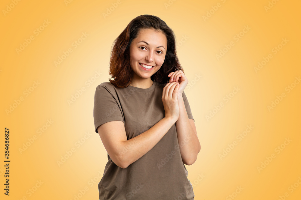 Portrait of a sweet smiling young Caucasian woman, modestly folded hands at the face. Yellow background. Human emotions, the concept of facial expression Portrait of a sweet smiling young Caucasian woman, modestly folded hands at the face. Yellow background. Human emotions, the concept of facial expression