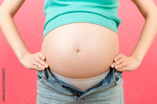 Cropped image of pregnant belly at colorful background with copy space. Expecting mother in opened jeans. Motherhood concept © sosiukin