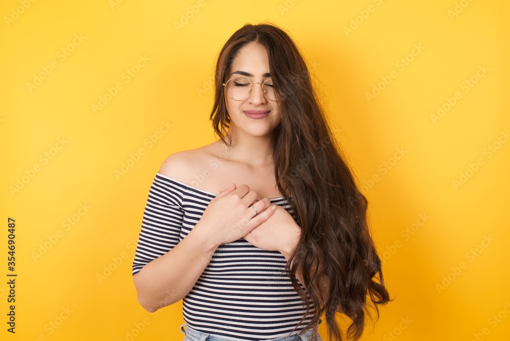 Faithful woman closes eyes and keeps hands on chest near heart, shows her kindness or favour, expresses sincere emotions, being kind hearted and honest. Body language and real feelings concept Faithful woman closes eyes and keeps hands on chest near heart, shows her kindness or favour, expresses sincere emotions, being kind hearted and honest. Body language and real feelings concept
