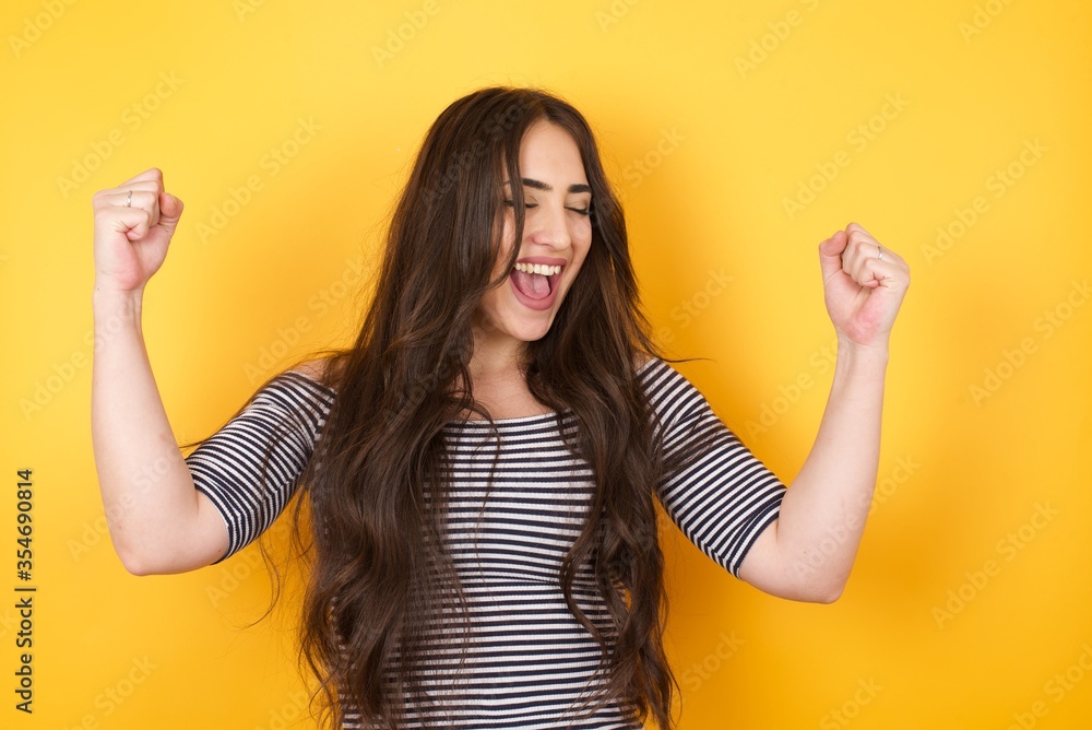 Caucasian brunette woman rejoicing her success and victory clenching her fists with joy. Lucky woman being happy to achieve her aim and goals. Positive emotions, feelings. Caucasian brunette woman rejoicing her success and victory clenching her fists with joy. Lucky woman being happy to achieve her aim and goals. Positive emotions, feelings.