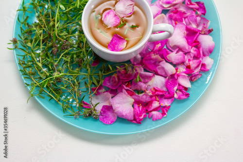 Homemade herbal tea in a white cup. Tea rose petals and thyme on a plate - ingredients for hot healthy drink 