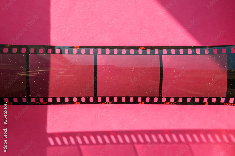 real 35mm filmstrip with empty frames on pink background, the sun is shining through empty film cells