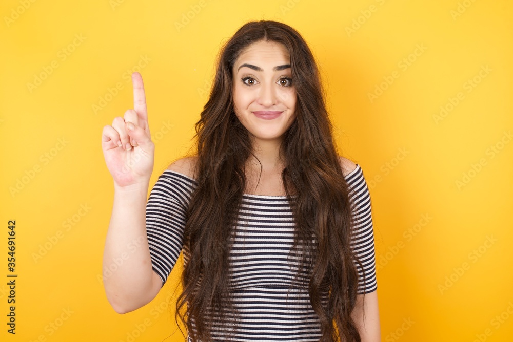 Young caucasian woman standing against yellow wall showing and pointing up with fingers number one while smiling confident and happy.
