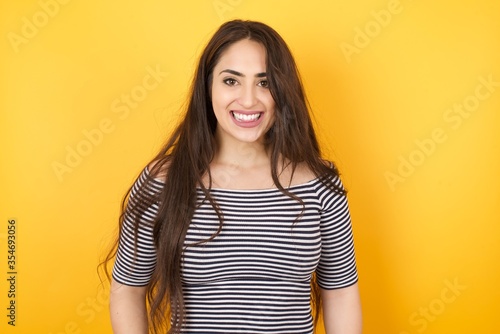 Beautiful Young caucasian woman with happy and funny face smiling and showing tongue. Wearing casual clothes and standing against gray studio background.