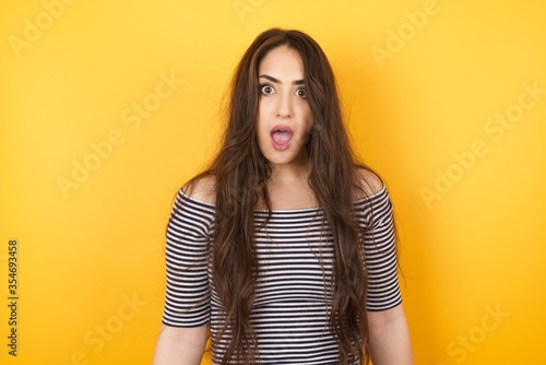 Emotional attractive female with opened mouth expresses great surprisment and frighteness, poses against white concrete background, stares at camera. Unexpected shocking news and human reaction.