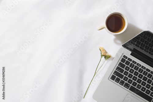 Top view of morning tea in voile fabric background with a laptop, mug of tea and a flower with space for text.