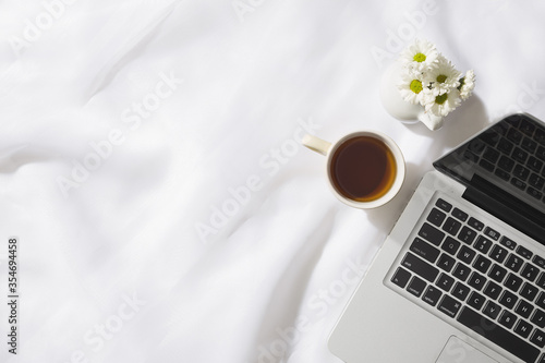 Top view of morning scene in voile fabric background with a notebook, mug of tea and a vase of white flowers with space for text.