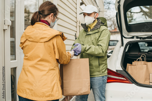 delivery man in a medical mask and gloves delivers the parcel in a craft package to the woman. Quarantine, coronavirus, isolation.