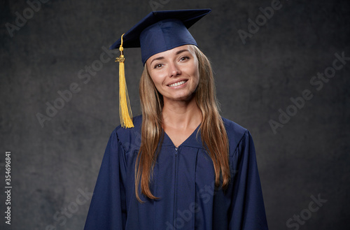 Happy young woman graduate wearing blue cap and gown looking straight