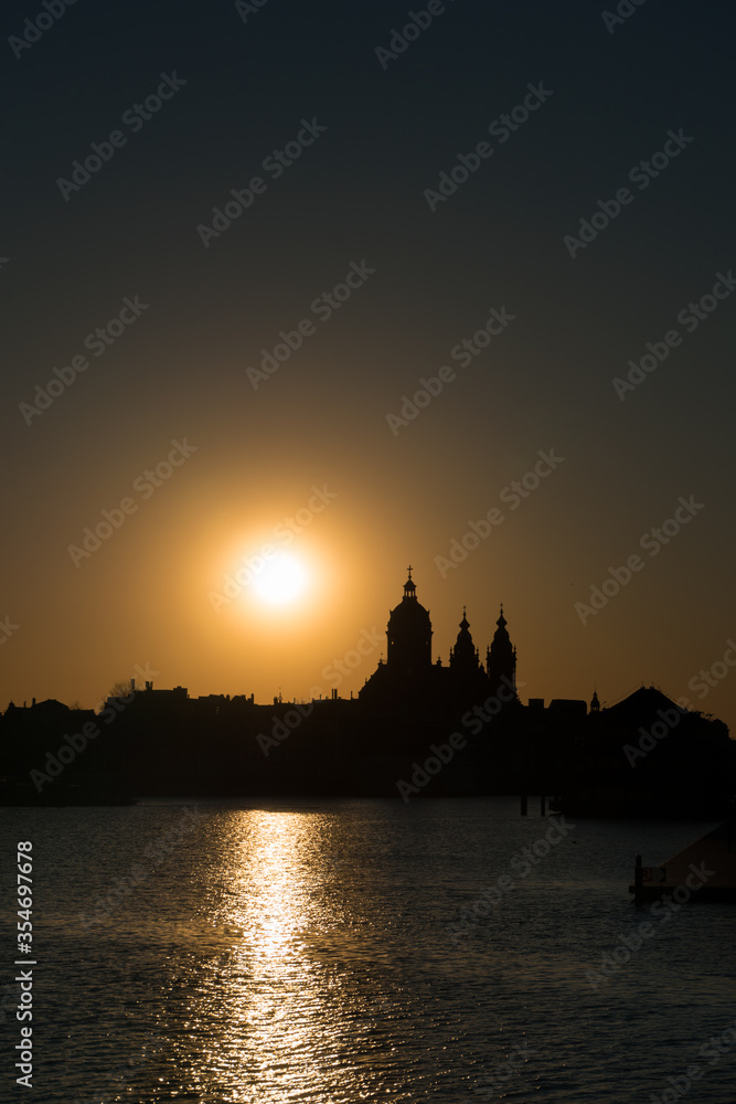 Neo-Baroque Basilica of Saint Nicholas silhouette at the sunset against orange sky with a sun setting behind in Amsterdam