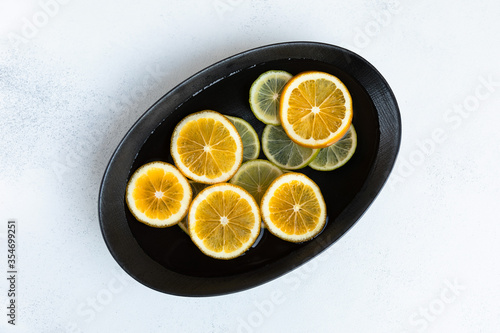 fresh and juicy sliced lemon and lime slices in water  in a black bowl on a white background  citrus background. beauty and health concept.