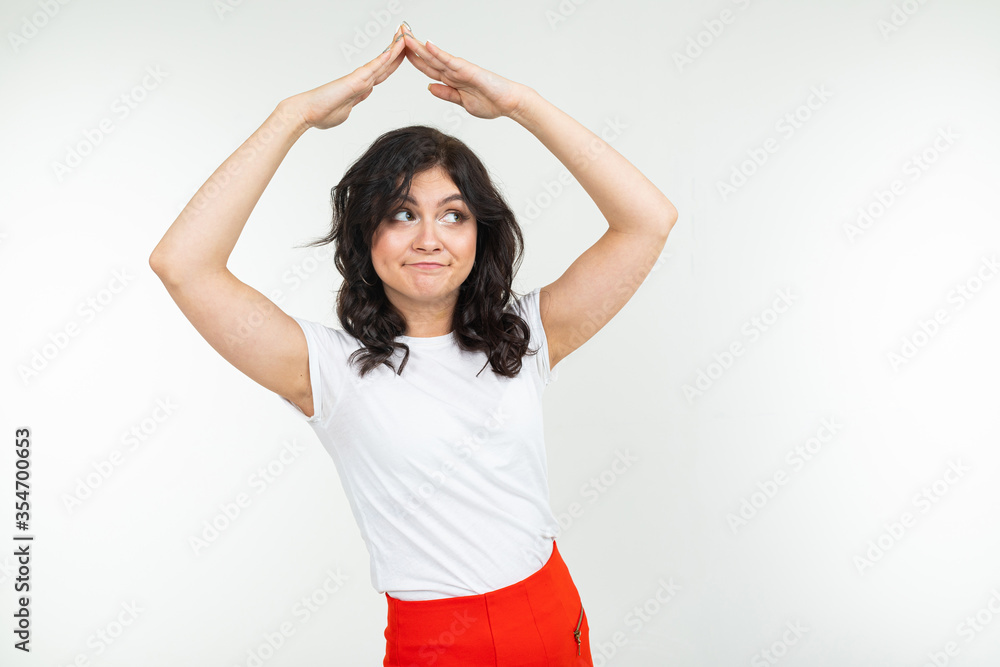 girl shows a safety sign while holding her hands over her head in the form of a roof on a white studio background girl shows a safety sign while holding her hands over her head in the form of a roof on a white studio background