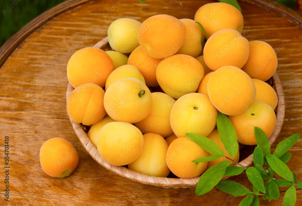 Ripe fresh apricots and leaves in wicker plate on wooden background, close up. Ripe fresh apricots and leaves in wicker plate on wooden background, close up.