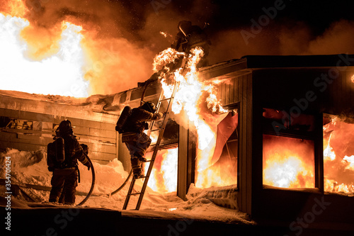 Huge fire blazing in commercial building and firefighter on a roof in winter condition Fototapeta