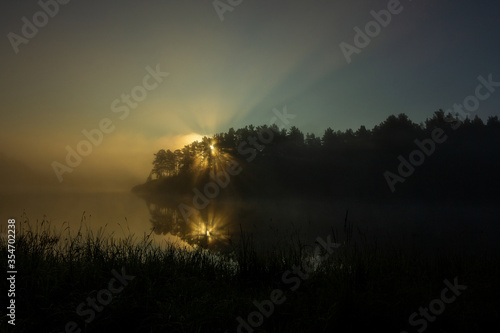 Fantastic foggy river with grass in the sunlight. Sun beams through tree. Dramatic colorful scenery. Beauty world.