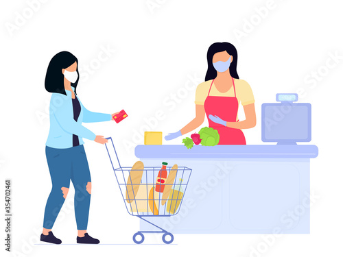 Woman in protective medical mask with shopping trolley pays with credit card at cash desk in supermarket. Quarantine of the coronavirus covid-19 epidemic