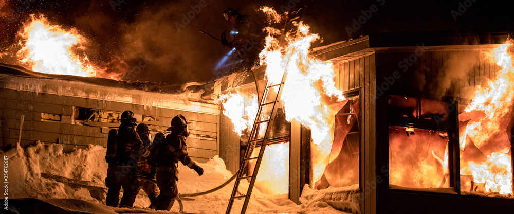 Huge fire blazing in commercial building and firefighter on a roof in winter condition. - obrazy, fototapety, plakaty 