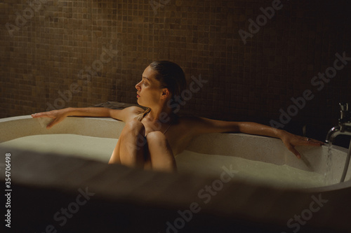 Beautiful smiling Caucasian woman posing with wet hair at bathroom, relaxing in the bath in the bathroom. young woman lying in bathtub. .woman taking a bath, personal care photo