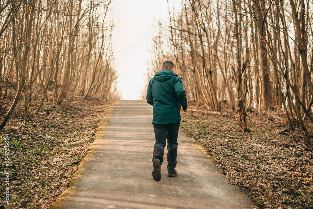 Fototapeta premium Portrait young handsome white brunette man running around in dark green sports jacket in park in spring. Healthy lifestyle, european, sneakers, sports pants, park, city, healthy, strong