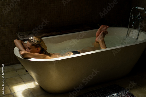 Beautiful smiling Caucasian woman posing with wet hair at bathroom, relaxing in the bath in the bathroom. young woman lying in bathtub. .woman taking a bath, personal care photo