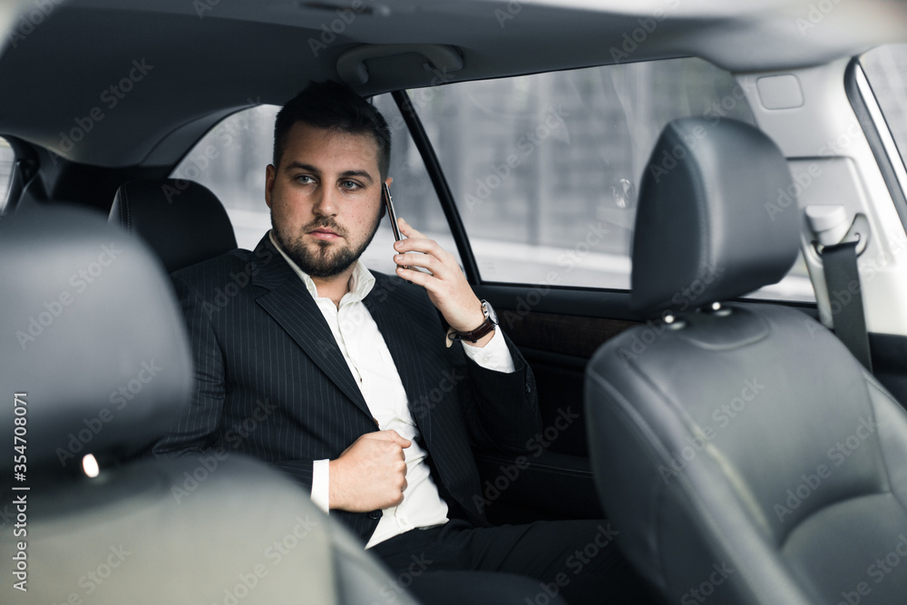 Handsome caucasian businessman driver inside in vehicle with coffee and gadget and check mail and talking with partners Handsome caucasian businessman driver inside in vehicle with coffee and gadget and check mail and talking with partners