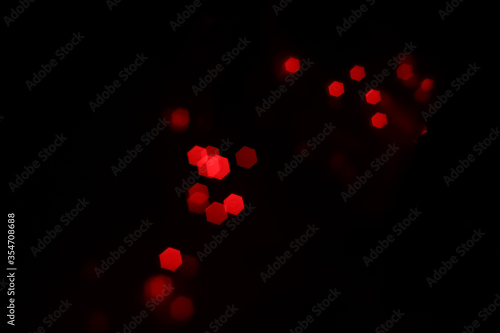 Red hexagonal bokeh lights on dark background from unfocused macro, created with red fairy lights and a vintage lens. 