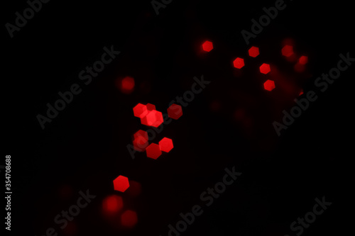 Red hexagonal bokeh lights on dark background from unfocused macro, created with red fairy lights and a vintage lens. 