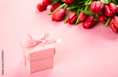 Gift box with a pink ribbon in white polka dots on a background of a bouquet of red tulips with free space for text. Wallpaper or banner for gift shop, flower shop or jewelry store. © Hanna