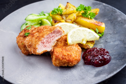 Traditionelles frittiertes Wiener Schnitzel von Kalb mit Bratkartoffel und Gurkensalat angeboten als closeup auf einem Modern Design Teller