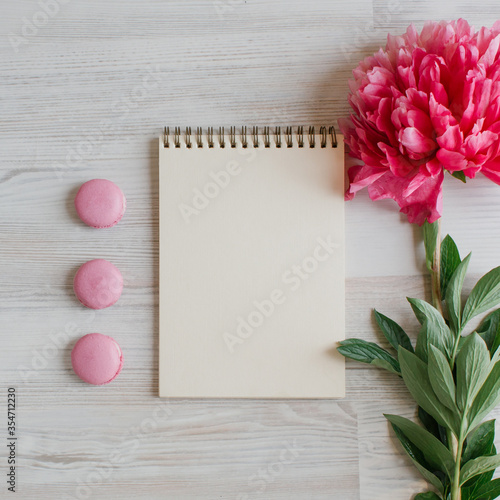 Fototapeta Naklejka Na Ścianę i Meble -  A blank notebook surrounded by pink peony flower and tasty sweet macarons,  a light wooden background, To-do list, plans, dreams. Top view, Vintage toned. Copy space for text