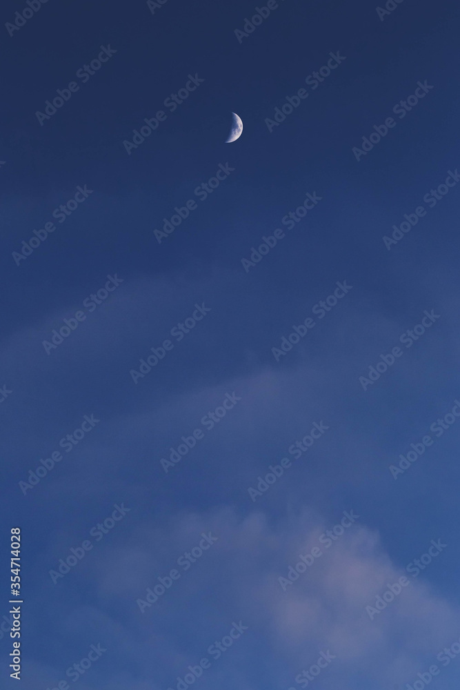 Vertical skyscape, blue sky with soft cluods and a crescent white and shining moon. Vertical skyscape, blue sky with soft cluods and a crescent white and shining moon.