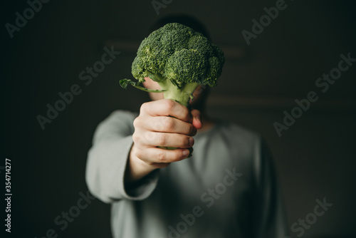 Man holding broccoli in his hand on a gray background. Healthy raw food, snack, green vegetables.
