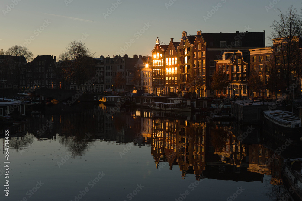 characteristic Dutch houses illuminated by the sun rising along the waalseilandgracht canal (Nieuwmarkt en Lastage district), closed to central station in Amsterdam city, Netherlands, Holland, Europe.